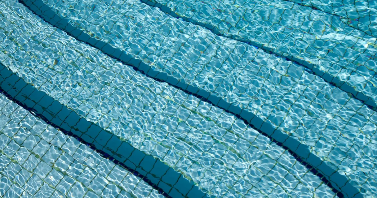 Água clara de uma piscina com azulejos azuis, ilustrando como limpar piscina